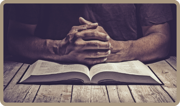 Image of a person at prayer, hands resting on the Bible, embodying the devotion to Scripture and belief in the power of Jesus Christ that is central to Imitatio's Statement of Faith.